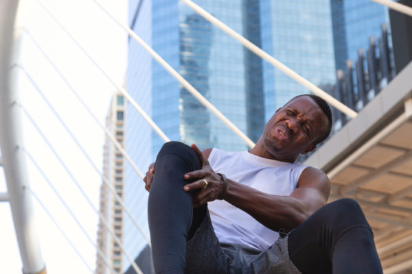 A man holds his knee in pain while outside in the city