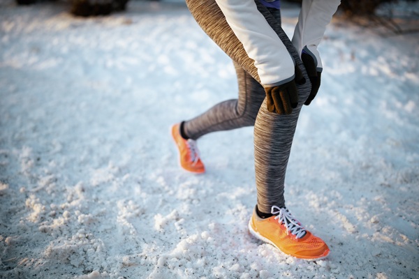 A person in athletic gear clutching their knee while standing on a snowy path.