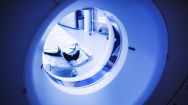 A view looking through the circular opening of a modern MRI or CT scanner, showing the patient table extending into the brightly lit, sterile medical room.